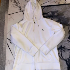 Vit Polo Ralph Lauren tröja - Säljer en stilren vit hoodie från Polo Ralph Lauren med dragkedja. Aldrig använd!