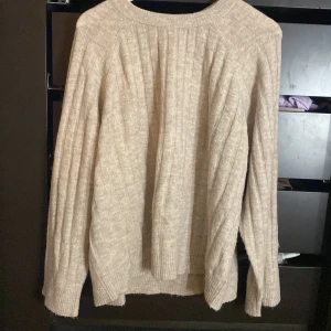 Beige stickad tröja från 157 - Mysig beige stickad tröja från 157 med ribbade detaljer. Perfekt för kyliga dagar med sin mjuka och bekväma passform. Tröjan har långa ärmar och en klassisk rund halsringning.