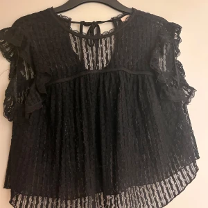Svart spetsblus från Nelly - Säljer en elegant svart spetsblus från Nelly i storlek XS. Blusen har korta ärmar med volangdetaljer och ett knytband i nacken. Perfekt för en stilfull look. En jätte fin blus som bara inte kommit till användning. Använd 1 gång och sedan glömt att använda. Frakt tillkommer, alltså jag betalar inte frakten.