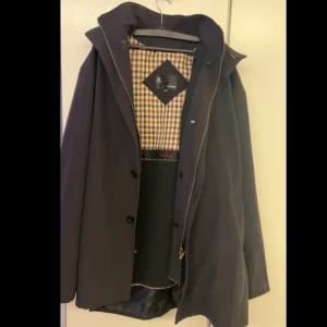 Svart rock från Polo Ralph Lauren - Snygg svart rock från Polo Ralph Lauren med klassiskt rutigt foder. Rocken har knappar och en stilren design som passar perfekt för höst och vinter. Den är långärmad och har en elegant krage. Funkar för XL också 