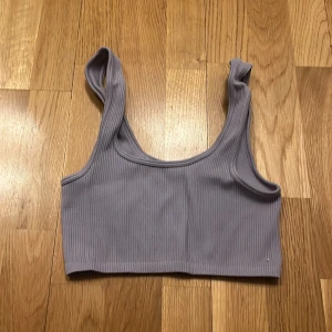 Ljuslila ribbad linnetopp - Säljer en snygg ljuslila ribbad linnetopp. Toppen har breda axelband och en enkel design som gör den perfekt för sommardagar. Den är tillverkad i ett mjukt och stretchigt material för en bekväm passform.