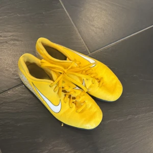 Gula Nike fotbollsskor - Säljer ett par gula Nike fotbollsskor med svart sula och vit Nike-logga. Skorna har snörning och är designade för inomhusbruk med en mönstrad yttersula för bra grepp.