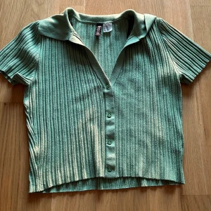 Grön ribbad t-shirt - En fin somrig, ribbad t-shirt från HM. Har både krage och knappar. Ganska kort modell, jag är 1,70 cm. Den är grönare i verkligheten än vad den är på bilden. 