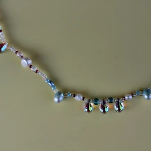 Färgglatt pärlhalsband med skimrande detaljer - Säljer ett unikt och färgglatt halsband med pärlor i olika nyanser av blått, vitt och rött. Halsbandet har skimrande droppformade detaljer som ger en extra touch av glamour. Perfekt för att liva upp vilken outfit som helst!