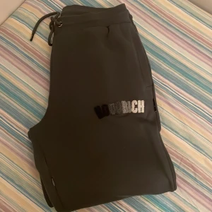 Svarta mjukisbyxor med broderad text - Säljer ett par mörk grå mjukisbyxor med en cool broderad textdetalj i vitt och svart. Byxorna har en bekväm passform och är helt nya 