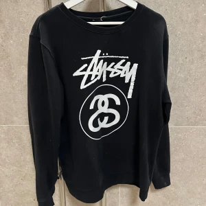 Svart sweatshirt från Stüssy - Säljer en svart sweatshirt från Stüssy med deras ikoniska logga i vitt på framsidan. Tröjan har långa ärmar och en rund halsringning. Perfekt för en avslappnad stil. Ovanlig design!