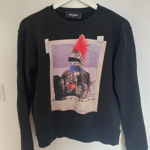 Svart tröja med tryck från DSQUARED2 - Säljer en svart tröja från DSQUARED2 med ett unikt tryck på framsidan. Tröjan har långa ärmar och en rund halsringning. Den är otroligt sparsamt använd och i jättebra skick! Inköpt för 2500kr på Farfetch.