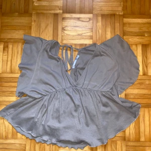 Beige blus med volangdetaljer - Beige blus med volangdetaljer och knytning i ryggen. Blusen har korta ärmar och en v-ringad design. Ställ gärna frågor!