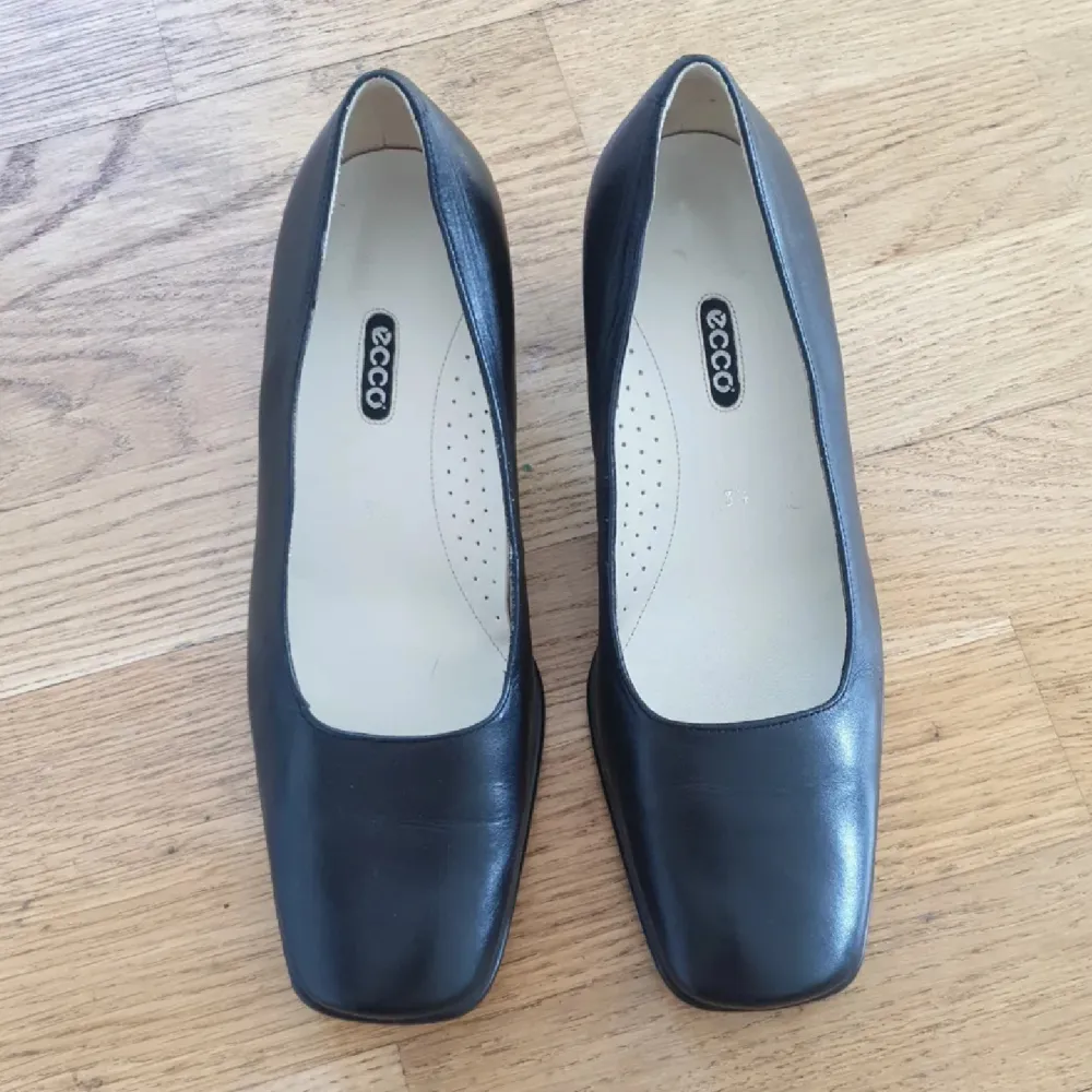 Eleganta svarta pumps från Ecco i skinn med en bekväm klack. Skorna har en klassisk design med fyrkantig tå och en stilren look. Perfekta för en chic och tidlös stil.. Kengät.