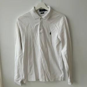 Vit långärmad pikétröja från Ralph Lauren - Säljer en stilren vit långärmad pikétröja från Ralph Lauren. Tröjan har en klassisk krage och knappar framtill. Den är i slim fit och har det ikoniska broderade logotypen på bröstet. Perfekt för en avslappnad men ändå elegant look.