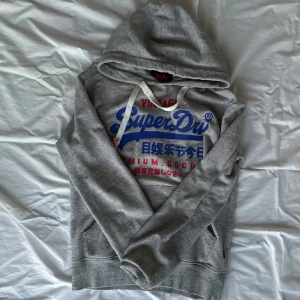 Grå hoodie från Superdry - Säljer en grå hoodie från Superdry. Snygg nu i vår/vinter. Inga defekter på sig, priser ej hugget i Sten! Kom med frågor vid funderingar!
