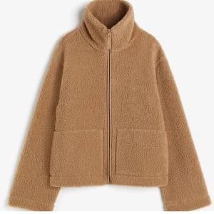 H&M Teddy jacka  - Mysig beige teddyjacka med dragkedja och hög krage. Perfekt för kyliga dagar med sin fluffiga och varma design. Jackan har två stora fickor framtill och långa ärmar.