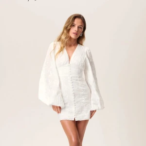 Vit klänning från Adoore - INTRESSEKOLL! Elegant vit klänning från Adoore med v-ringning och långa puffärmar. Klänningen har en figurnära passform och knappar framtill. Perfekt för studenten! Använd 1 gång, nyskick.