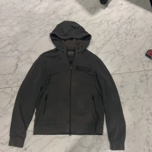 Mörk grön hoodie från aeronautica militare  - Säljer en mörkgrön huvjacka från Aeronautica militare med dubbel dragkedja och långa ärmar. Jackan har en stilren design med ribbade muddar och en praktisk huva. Perfekt för en casual men mysteriös look. Luft indrag under armarna och två fickor med dragkedjor. Pris lätt diskuterbart vid snabb affär 