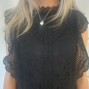 Svart spetsblus - Snygg svart spetsblus med detaljerad spetsdesign och ärmlös stil. Perfekt för en elegant look med fina mönster och en feminin touch.