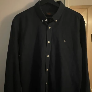 Mörkblå skjorta från Morris - Snygg mörkblå skjorta från Morris med broderad detalj på bröstet. Skjortan har långa ärmar och knappar framtill. Perfekt för en stilren look.