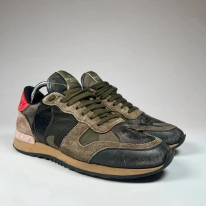 Valentino Garvani Rockrunners i camouflage - Snygga Valentino Rockrunner sneakers i en cool mix av färger. Skorna har ett camouflage-mönster i grönt och svart med detaljer i rött och beige. Tillverkade i en kombination av skinn och mocka med snörning framtill. Skick: 3/5