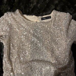 Glittrig kortärmad topp  - Säljer en glittrig kortärmad topp. Toppen har en öppen rygg med knytband och är täckt av paljetter som ger en festlig look. Perfekt för en utekväll eller speciella tillfällen. ✨