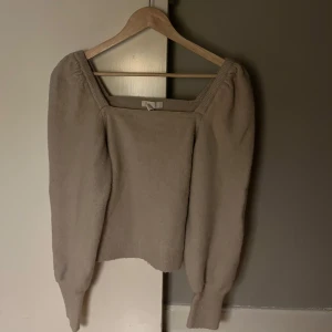 Beige stickad tröja - Säljer en stilren beige stickad tröja med fyrkantig halsringning. Tröjan har långa ärmar och en mjuk, bekväm passform. 