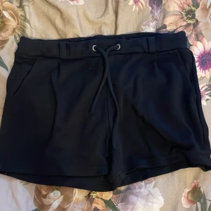 Svarta shorts från QueenZ - Snygga svarta shorts från QueenZ med dragsko i midjan för en bekväm passform. Tillverkade i en mix av viskos, nylon och elastan vilket ger en mjuk och stretchig känsla. Perfekta för en avslappnad stil.