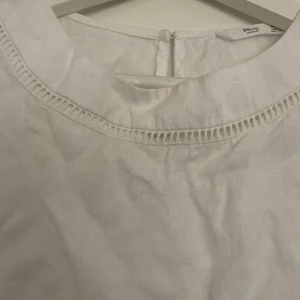 Vit blus  - Säljer en stilren vit blus. Blusen har korta ärmar och en rund halsringning med dekorativ kant. 