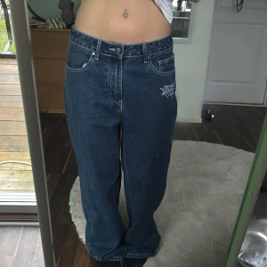 Ed Hardy baggy jeans med tryck - Coola jeans från Ed Hardy x Urban Outfitters med unikt tryck på baksidan. Mörkblå denim med text och hjärtdetaljer. Perfekta för dig som vill sticka ut med en edgy stil. Använda 2-3 gånger så väldigt bra skick. 