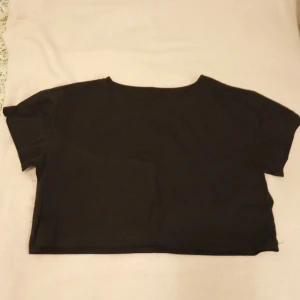 Svart croppad topp från Gina Tricot - Säljer en stilren svart croppad topp från Gina Tricot. Perfekt för en avslappnad look. Toppen har korta ärmar och en enkel design som gör den lätt att matcha med olika outfits.