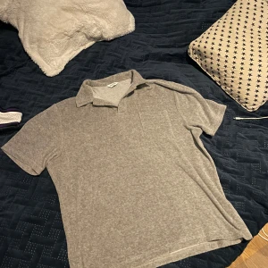 Grå pikétröja från East West - Säljer en stilren grå pikétröja från East West. Tröjan har korta ärmar och en klassisk krage. Perfekt för en avslappnad look.