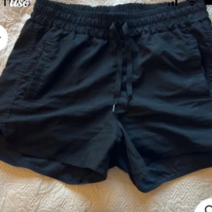 Svarta shorts med dragsko - Snygga svarta shorts med elastisk midja och dragsko för justerbar passform. Perfekta för en avslappnad stil. De har en enkel design utan mönster och är gjorda i ett lätt material.