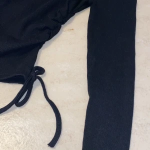 Svart ribbad topp med knyt - Snygg svart ribbad topp med långa ärmar och knytning i midjan. Aldrig använd. 