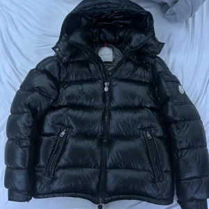 Svart dunjacka från Moncler - Säljer en snygg svart pufferjacka från Moncler. Jackan har en glansig finish och är utrustad med dragkedja och huva. Perfekt för kyliga dagar. Moncler-loggan syns tydligt på ärmen. Kvitto ingår på äktenskap! (Byten funkar också)