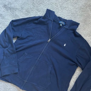 Mörkblå hoodie från Ralph Lauren - Säljer en snygg mörkblå hoodie från Ralph Lauren med dragkedja och det klassiska logotypbroderiet på bröstet. Tröjan är i storlek XL men sitter som M!  Nypris 2250kr