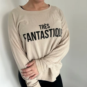 Beige långärmad tröja med text - Säljer en beige långärmad tröja med texten 'TRÈS FANTASTIQUE' i svart på framsidan. Super mysig och bekväm🤍🤍