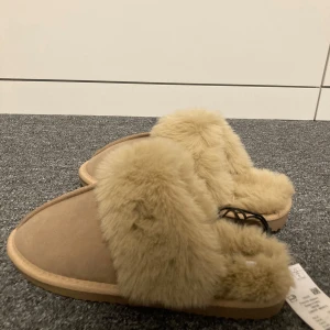 Beige tofflor med fuskpäls - Mysiga beige tofflor med mjuk fuskpäls. Storlek 38/39 