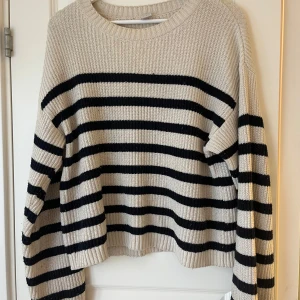 Randig stickad tröja från Lindex - Säljer en fin stickad tröja från Lindex i beige med svarta ränder. Tröjan har en rund halsringning och långa ärmar, perfekt för kyligare dagar. Passar även som xs💗