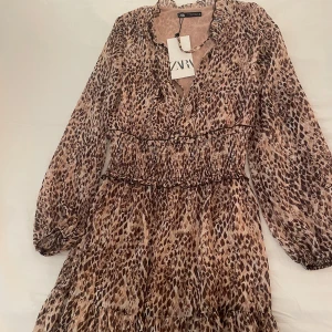 Mönstrad klänning från Zara - Säljer en superfin mönstrad klänning från Zara i storlek XS. Klänningen har ett leopardmönster i bruna och beige toner, med långa ärmar och en smickrande v-ringning. Perfekt för både vardag och fest!