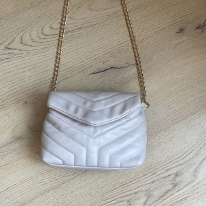 Vit quiltad axelväska med guldkedja - Säljer en superfin beige axelväska med quiltat mönster och guldkedja. Väskan har en praktisk dragkedja inuti och stängs med en tryckknapp. Perfekt för både vardag och fest! 👜✨Sälje pga av att den inte kommer till användning, använd endast 1 gång