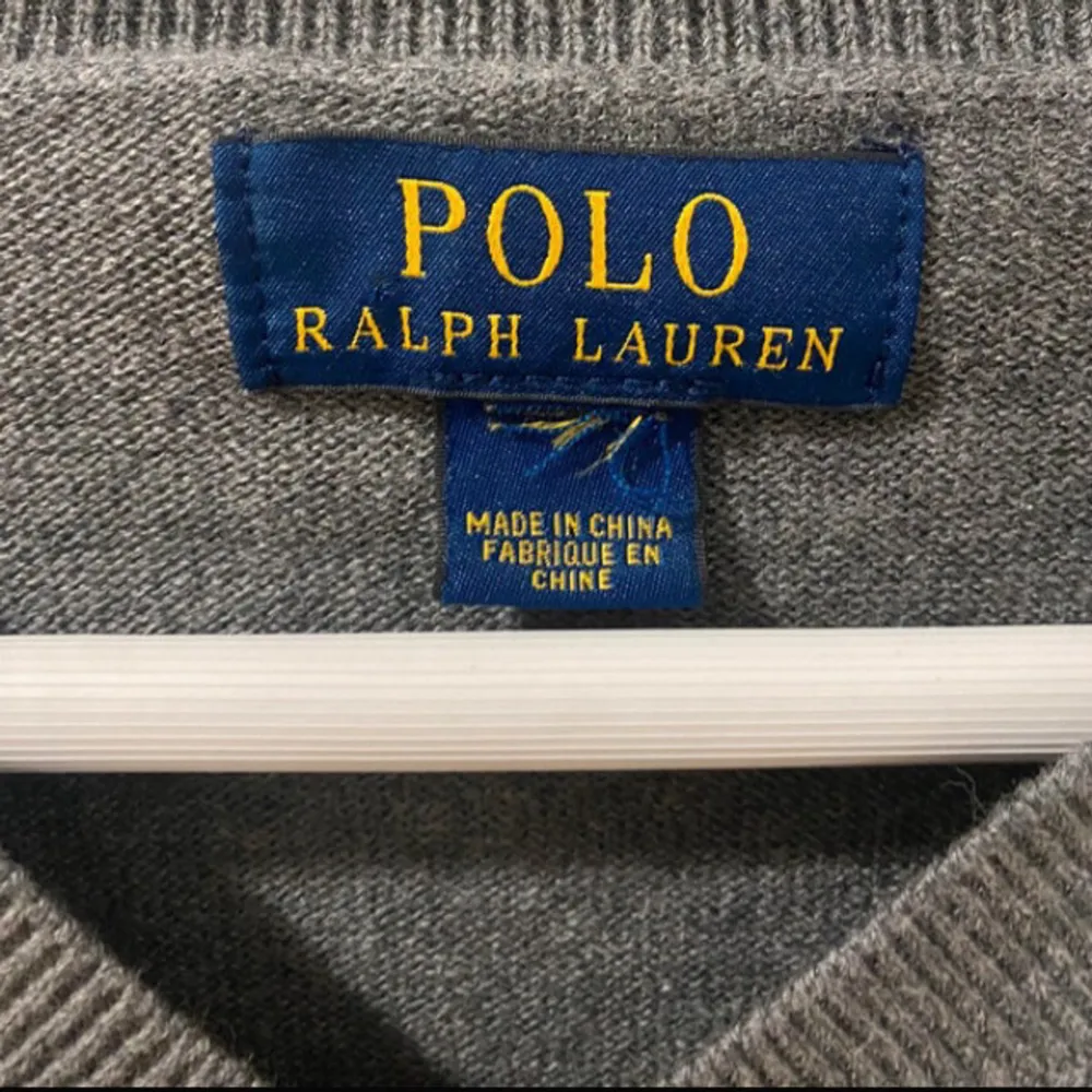 Säljer en stilren grå tröja från Polo Ralph Lauren i 100% bomull. Den har snygga bruna armbågslappar och en klassisk v-ringning. Perfekt för både höst och vår. Tröjan är i mycket bra skick och har den ikoniska broderade loggan på bröstet. Storlek M fast passar S.. Tröjor & Koftor.