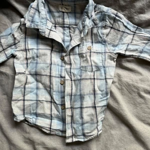 Rutig skjorta från Newbie - Säljer en superfin rutig skjorta från Newbie i storlek 86 för barn 12-18 månader. Skjortan har en mjuk och skön känsla med knappar framtill och en liten bröstficka. Perfekt för både vardag och festliga tillfällen! 💙
