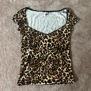 Leopardmönstrad topp från Nelly - Säljer denna populära, snygga, leopardmönstrad topp från Nelly i storlek S. Toppen har en v-ringad design och korta ärmar, perfekt för en utekväll eller fest. Materialet är mjukt och stretchigt för en bekväm passform. 🐆✨Endast provad så den är som ny💕hör gärna av dig vid intresse!