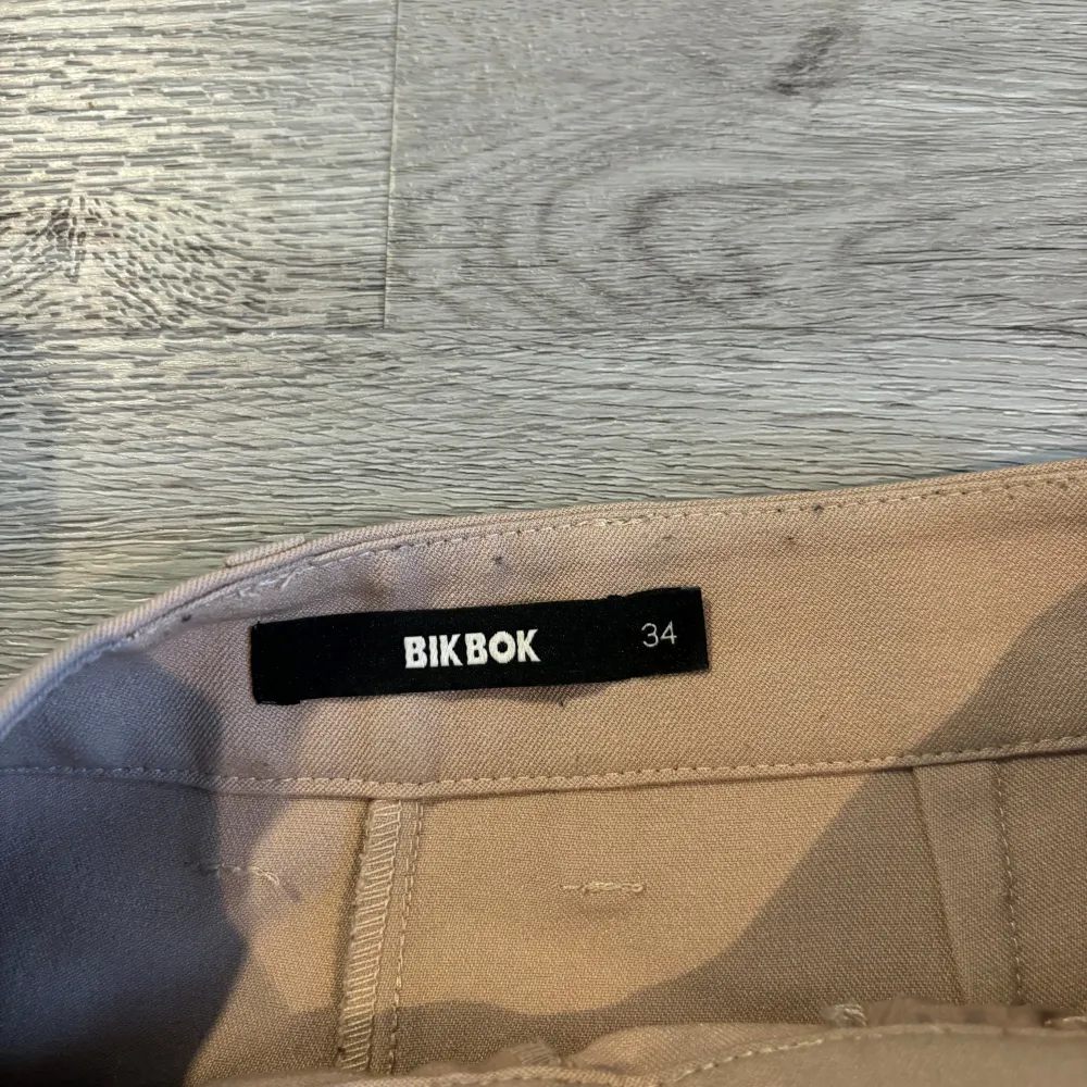 Säljer ett par snygga beige kostymbyxor från BikBok i storlek 34. De är högmidjade med en klassisk rak passform och har knäppning fram. Perfekta för både vardag och fest! 🕺. Jeans & Byxor.