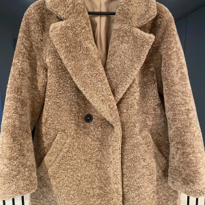 Beige/brun teddyjacka från H&M - Mysig teddyjacka från H&M i storlek S, passar även M då den är lite oversized. Perfekt för höst och vinter med sin fluffiga och varma design. Jackan har en klassisk krage och stängs med knappar framtill. Den är långärmad och har en avslappnad passform, vilket gör den idealisk för lager-på-lager-stil.