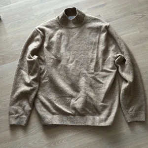 Beige ulltröja från Weekday strlk M - Säljer en mjuk beige polyester/ulltröja med högre krage från Weekday. Perfekt för kyliga dagar med sin ribbade polokrage och långa ärmar. Strlk M.