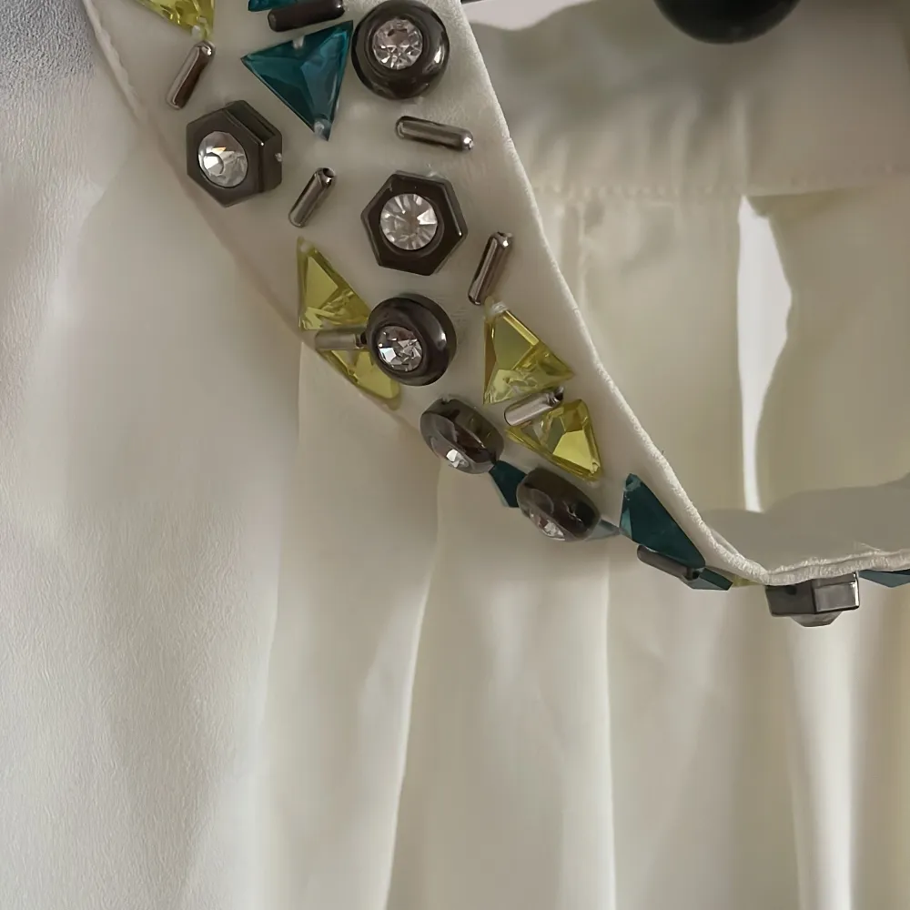 Säljer en vit blus med korta ärmar och en unik krage dekorerad med färgglada stenar och nitar i gult och turkost. HM, st.36 , Nytt!Perfekt för att ge en extra touch till din outfit. Passar både till vardags och festliga tillfällen.. Yläosat.