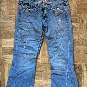 Säljer ett par blå jeans från True Religion i bra skick. De har en snygg slitning och coola detaljer med knappar och broderi på bakfickorna. Perfekta för en avslappnad stil. Passar bra till både vardag och fest! Kontakta gärna innan köp. 