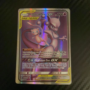 Mewtwo & Mew GX Pokémonkort - Säljer ett Mewtwo & Mew GX TAG TEAM Pokémonkort med 270 HP. Kortet har en holografisk yta och visar de två Pokémon i en kraftfull pose. Perfekt för samlare eller spelare som vill stärka sin kortlek med en stark TAG TEAM-kombination.