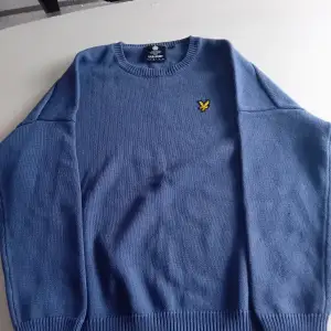 Säljer en snygg blå tröja från Lyle & Scott i storlek L. Den har en klassisk rund hals och ett gult broderat emblem på bröstet. Perfekt för både höst och vår. Tröjan är i mycket bra skick och gjord av mjukt material som känns skönt mot huden.