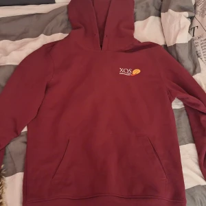 Vinröd hoodie från XQS - Säljer en snygg vinröd hoodie från XQS med broderad logga 'Chili Mango' på bröstet. Den har en klassisk känguruficka och är perfekt för kyliga dagar. Passar både till vardags och chillkvällar. Skön passform och använd typ 5 gånger, men har dock inga snören till luvan.