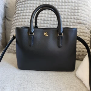 Ralph Lauren väska - Ralph lauren väska(äkta)köpt på zalando. Helt perfekt storlek(mellanstor)inte för stor och samtidigt inte för liten. Nyskick då den aldrig använts. Långa väskbandet är avtagbart. Tags och allt finns kvar och dustbag medföljes. Möts upp i Stockholm gullmarsplan.