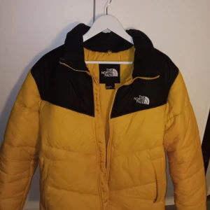 Gul och svart pufferjacka från The North Face - Säljer en skit snygg gul och svart north face puffer jacka jackan är använd i ungefär 1 vinter säsong den har även en liten reva vid armen men den är knappt synlig jackan är också nyligen hand tvättad med skicklighet